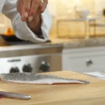 A chef sprinkles salt on a branzino fillet