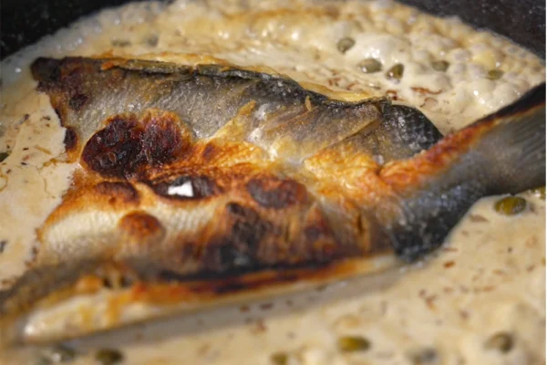 Butterflied-Branzino-Cooked-Plated A crispy butterflied branzino fillet in a pan with caper sauce