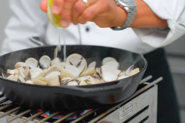 Frozen-Clams-Wholesale A chef squeezes a lemon over white clams cooking in a pan with white wine