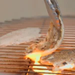 A chef flips branzino fillet on a grill