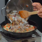 Seafood medley is added to rice that is cooking in a pot