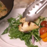 Grilled and stuffed calamari tubes are plated over a bed of arugula