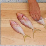 A chef scores whole yellowtail snapper on a cutting board